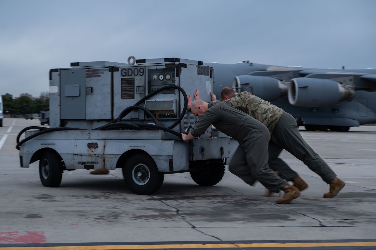 Capt. Ben Bertelson, left, and 1st Lt. Garrett Watts, right, 3rd Airlift Squadron C-17 Globemaster III pilots, push an external power cart during rapid departure training at Dover Air Force Base, Delaware, March 10, 2023. Team Dover Airmen participated in a week-long readiness training exercise during which the 3rd AS practiced rapid departure capabilities, further enabling their rapid response in a fast-paced threat environment. (U.S. Air Force photo by Senior Airman Cydney Lee)