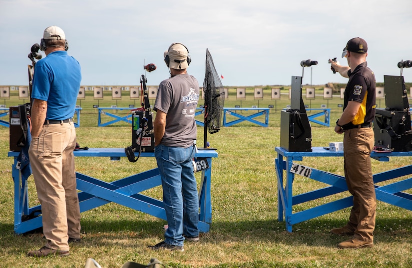 Multiple men firing pistols on outdoor pistol range.