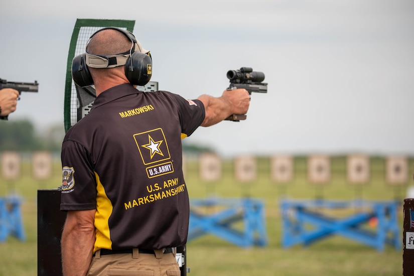 Man in USAMU shooting uniform firing pistol on outdoor pistol range.