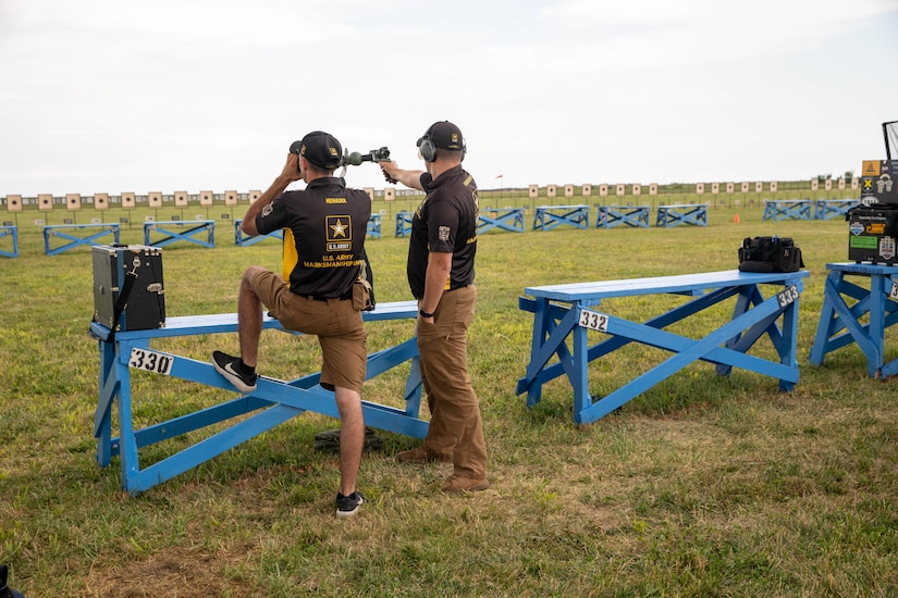 Men in USAMU shooting uniforms firing pistol on outdoor pistol range.