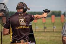 Man in USAMU shooting uniform firing pistol on outdoor pistol range.