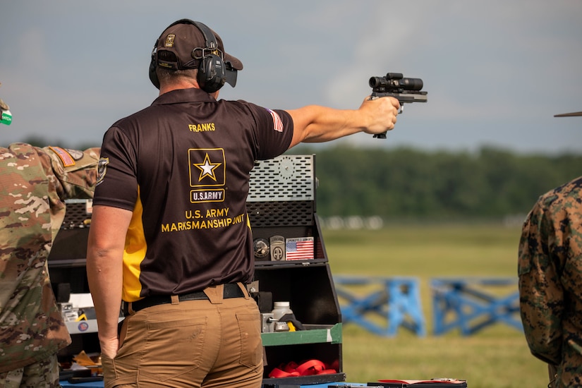 Man in USAMU shooting uniform firing pistol on outdoor pistol range.