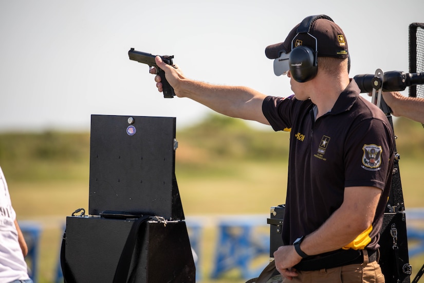 Man in USAMU shooting uniform firing pistol on outdoor pistol range.