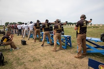 Multiple men in shooting uniforms firing pistol on outdoor pistol range.