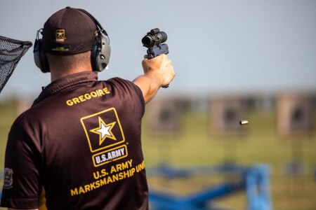 Man in USAMU shooting uniform firing pistol on outdoor pistol range.