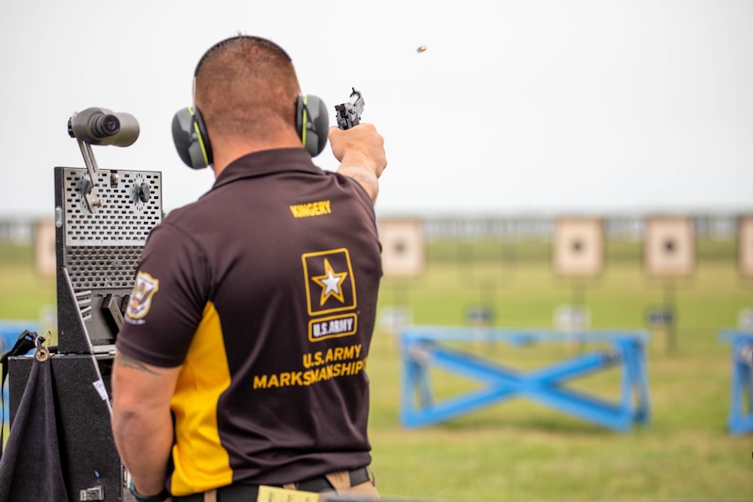 Man in USAMU shooting uniform firing pistol on outdoor pistol range.