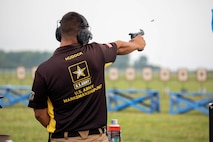 Man in USAMU shooting uniform firing pistol on outdoor pistol range.