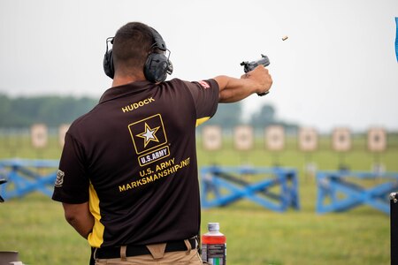 Man in USAMU shooting uniform firing pistol on outdoor pistol range.