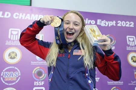 Woman in U.S.A. uniform celebrating with medals in front of event sign.