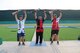 3 men in U.S.A. uniforms celebrating with shotguns on outdoor podium.