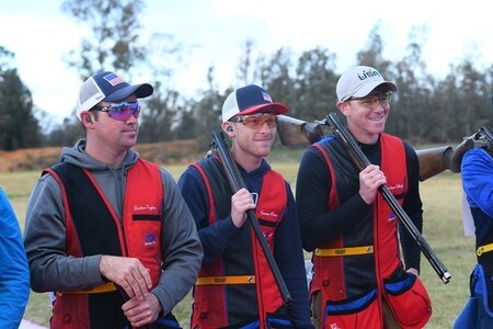 Men in shooting uniforms posing with their shotguns outside at event.