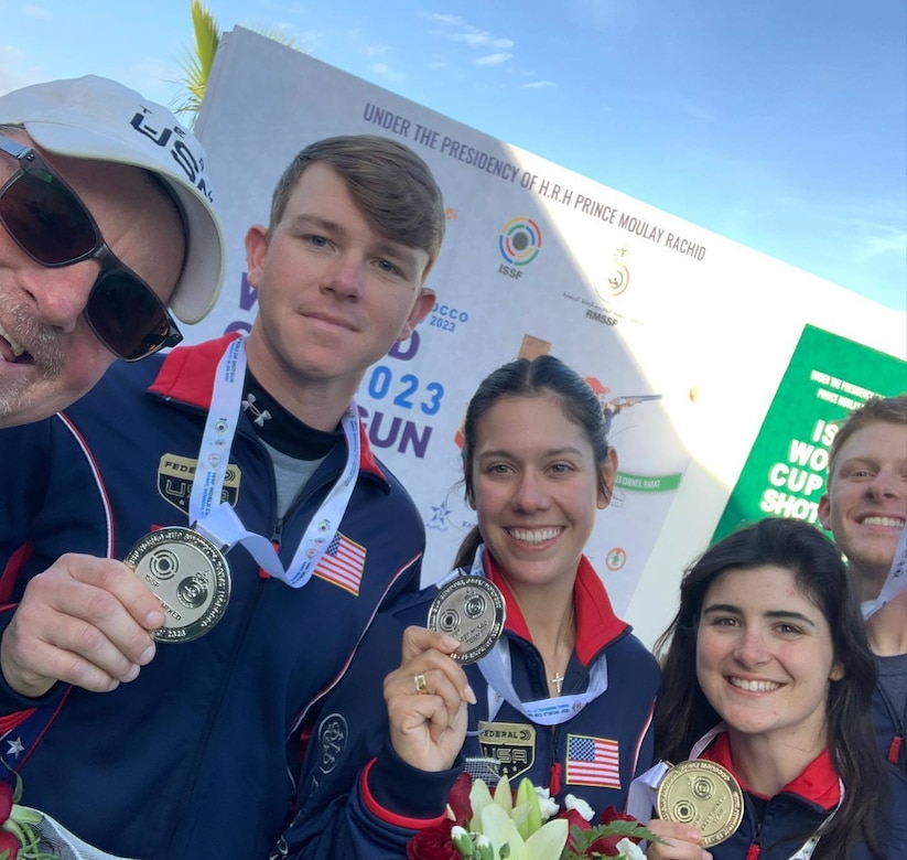 Men and women in U.S.A. uniform celebrating with medals in front of event banner.