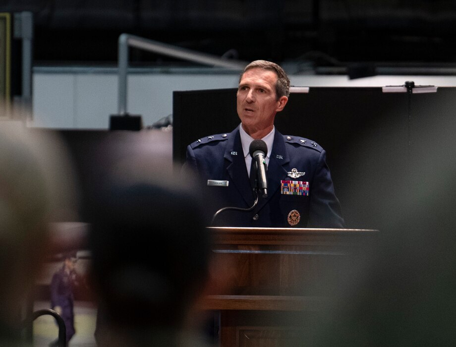 Man speaks at a podium. Some of his audience is in the foreground.