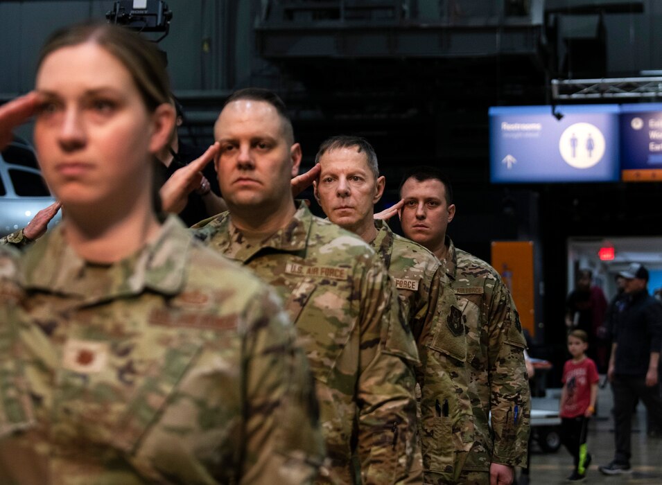 A line of Airman in camouflaged uniform stand facing the camera saluting.