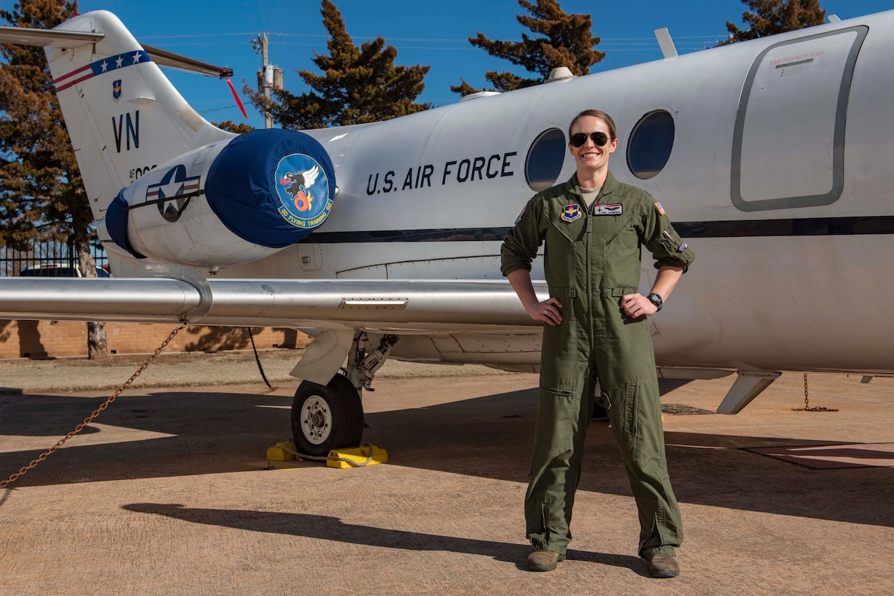 An Air Force pilot stands, smiling, with her hands on her hips.