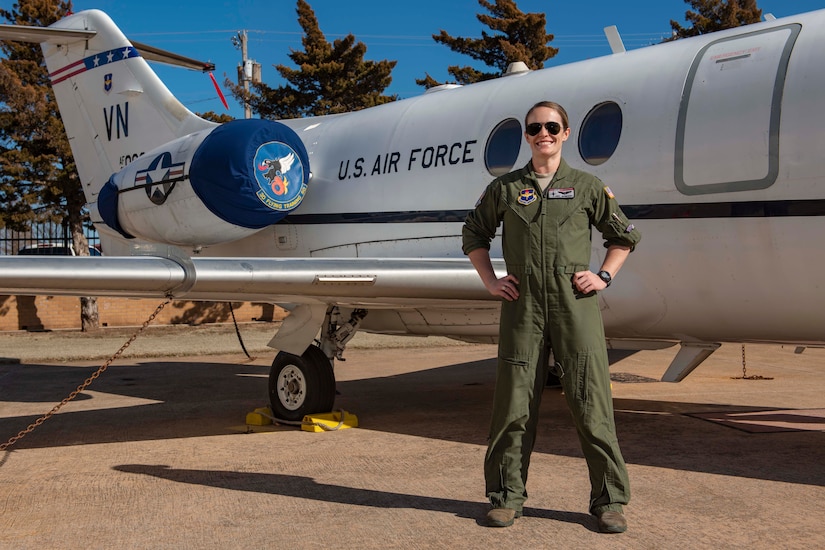 An Air Force pilot stands, smiling, with her hands on her hips.