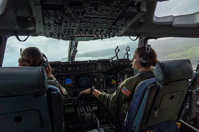 Two Air Force pilots are shown inside a military aircraft's cockpit.