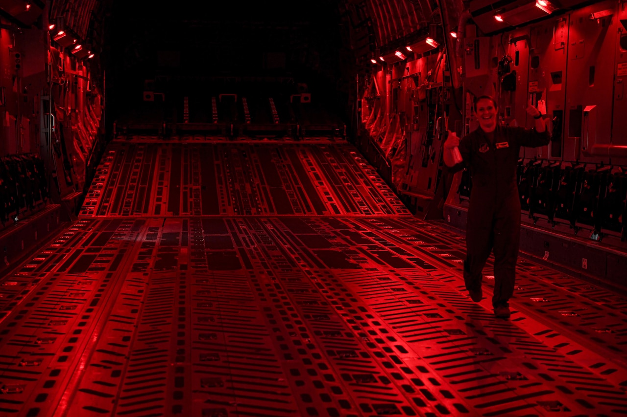 A pilot gives a thumbs up inside an aircraft's cargo area while illuminated in red.