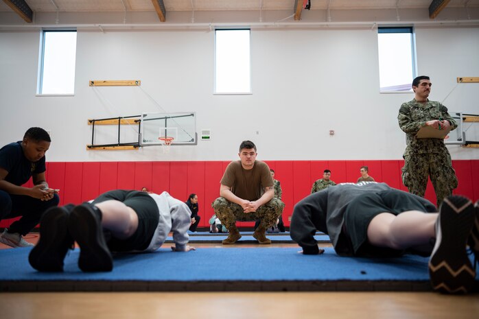 Sailors observe Junior Reserve Officers' Training Corps cadets’ pushups during the physical fitness assessment portion of a regional JROTC competition at Shelton High School in Shelton, Washington, Feb. 4, 2023. Active duty members from all service branches participated as judges for the competition, which brought local high school JROTC students together to compete in a series of four events including color guard, physical fitness, academics and a military-style ceremonial drill performance. (U.S. Navy photo by Mass Communication Specialist Seaman Sophia H. Brooks)