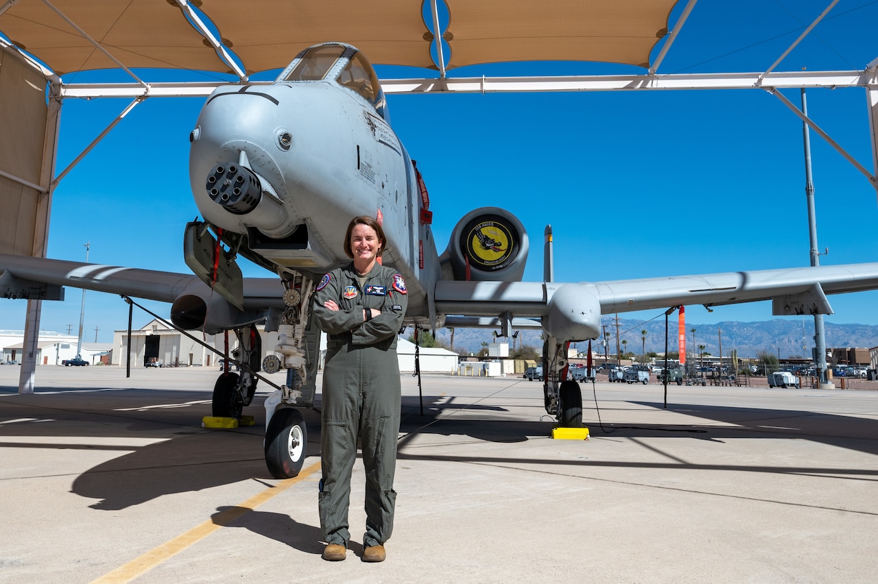 A woman poses for a photo while standing in front of a jet.