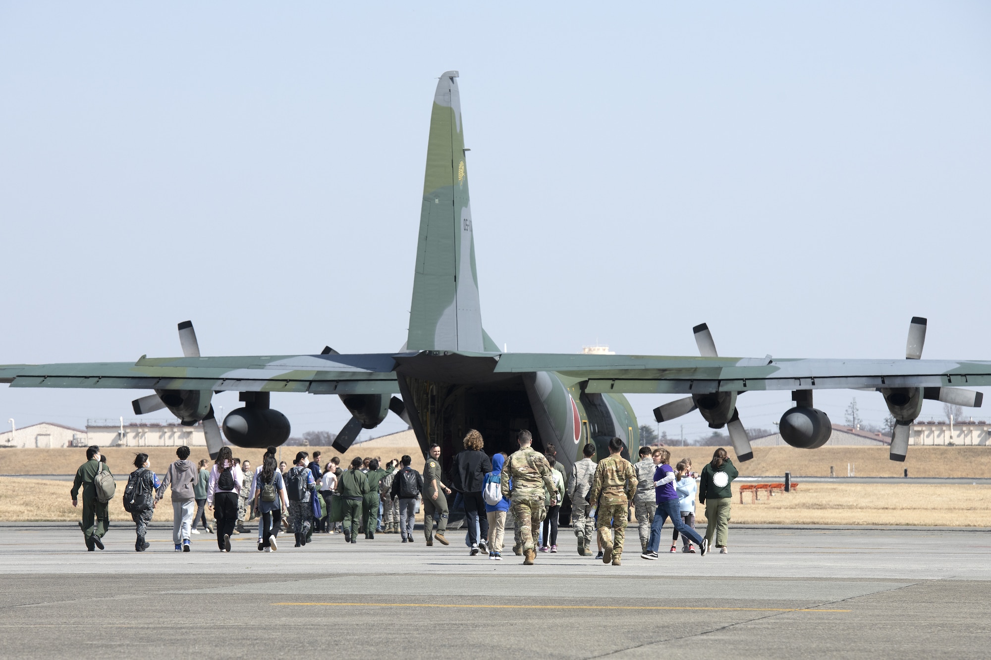 U.S. Air Force and Japan Air Self-Defense Force members walk with middle school and high school students toward a C-130H Hercules.