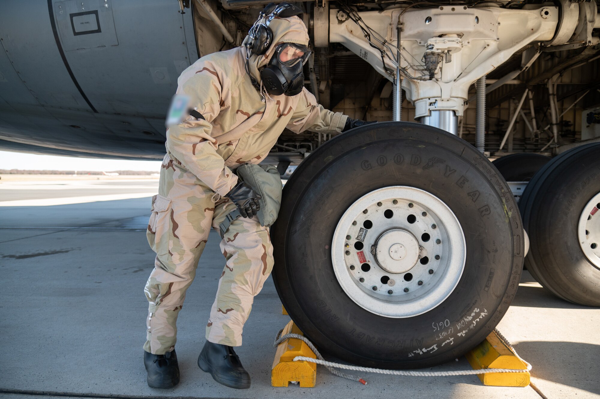 An Airman with the 512th Aircraft Maintenance Squadron chocks a C-5M Super Galaxy while wearing mission oriented protective posture gear during a readiness exercise at Dover Air Force Base, Delaware, March 8, 2023. The exercise tested the abilities of Dover AFB Airmen to generate, employ and sustain airpower across the world in a contested and degraded operational environment. (U.S. Air Force photo by Mauricio Campino) (Part of this image was blurred to conceal a security badge.)
