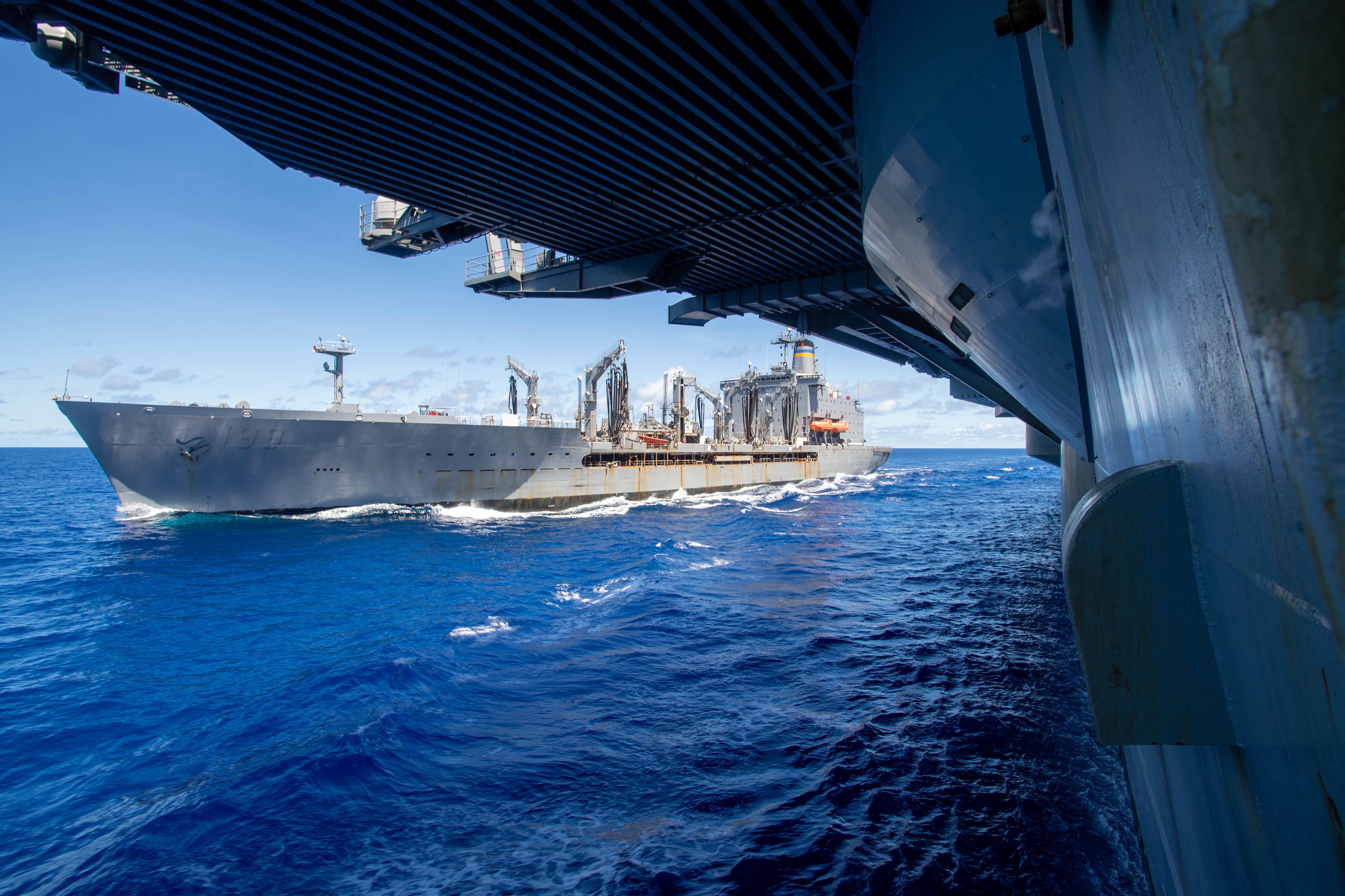 A Navy ship sails alongside another ship in the sea.