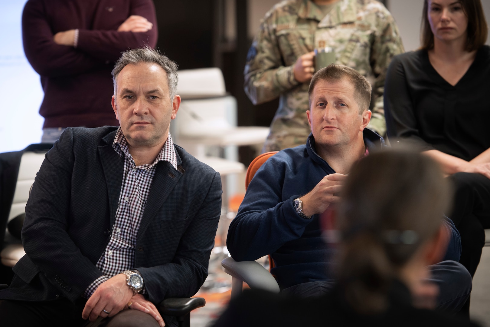 Two men in suits listen to briefing