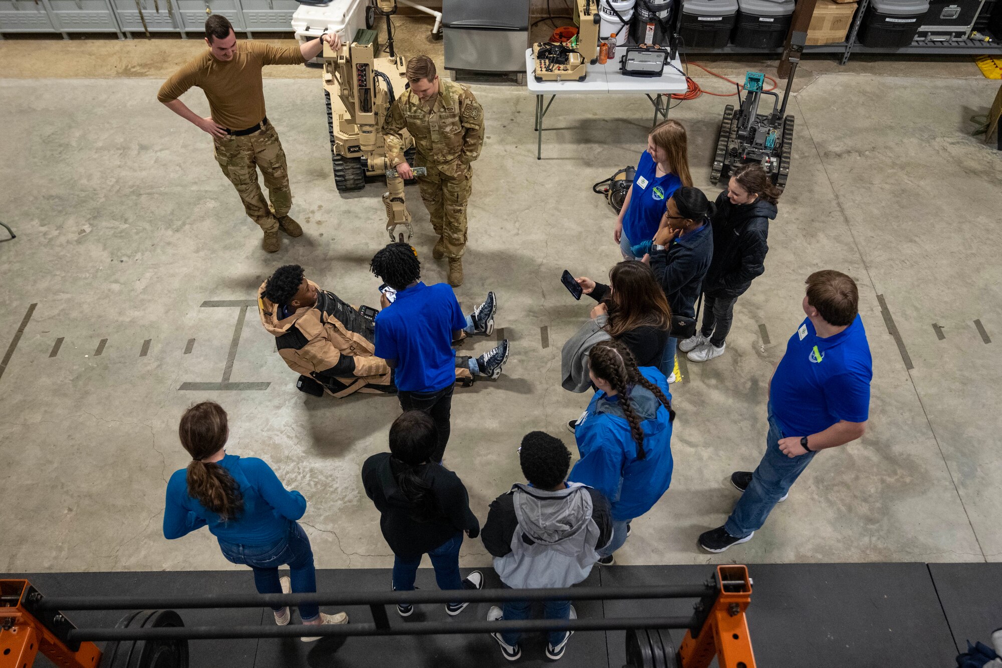 A student wearing a bomb suit tries to stand while other students look on.