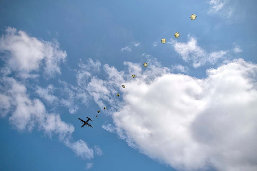 Paratroopers descend from a military aircraft.