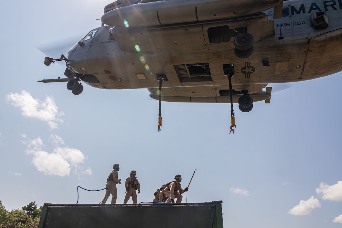 Marines prepare to attach heavy equipment to a military helicopter.