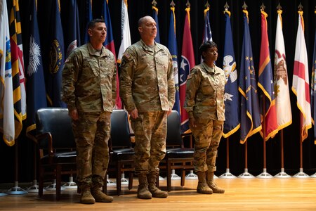 three people wearing u.s. army uniform stand in a group on a stage.