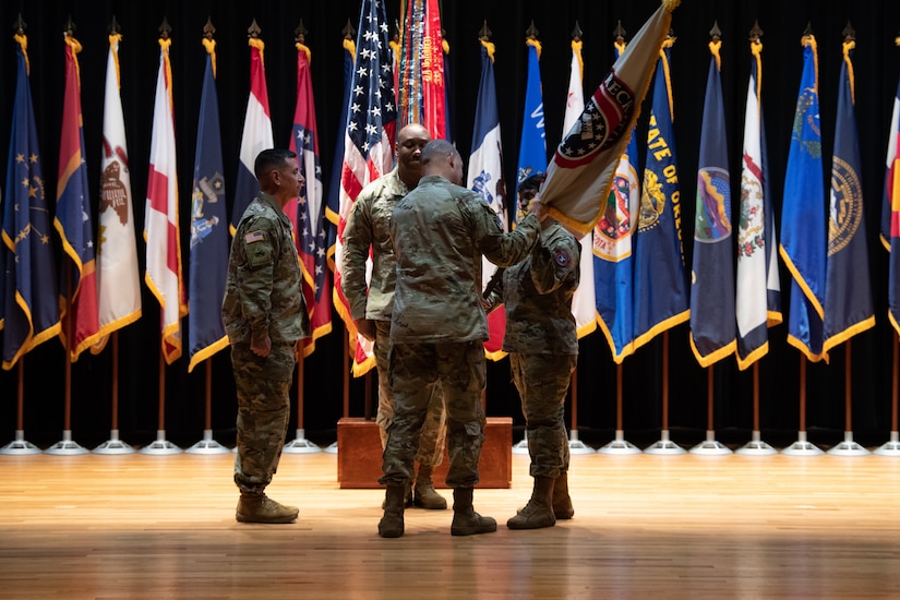 four people wearing u.s. army uniform stand in a group on a stage.