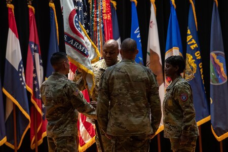 four people wearing u.s. army uniform stand in a group on a stage.