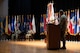 man wearing u.s. army uniform stands behind a podium and points at two people sitting in chairs.