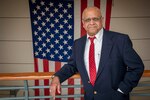 Mohamed Ahmed, an electrical engineer in Naval Undersea Warfare Center Division Newport’s Sensors and Sonar Systems Department, poses in front of an American flag on Nov. 16, 2022. The flag is a source of pride for Ahmed, who on Nov. 21, 2022, marked 50 years since arriving in the United States as a refugee from Uganda.