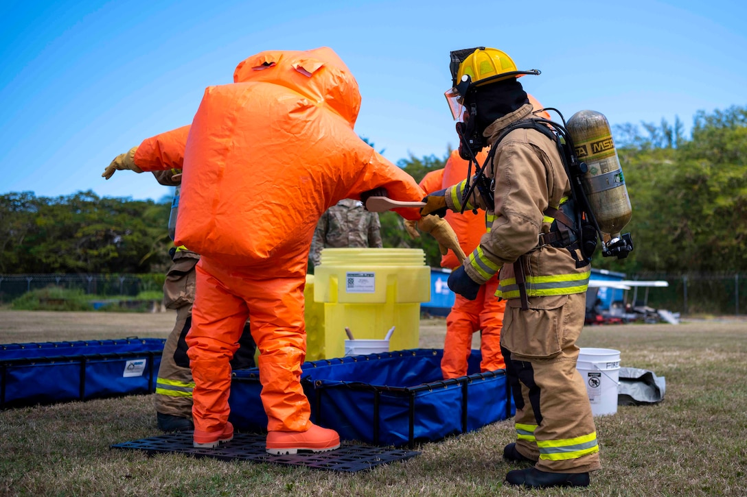An airman wearing fire protective equipment decontaminates another airman’s personal protective gear.