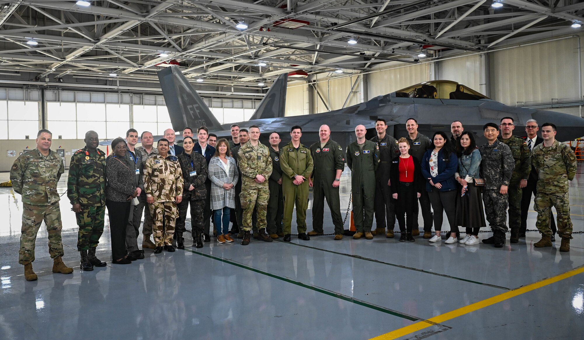U.S. Air Force personnel, international air attachés and spouses pose for a photo in front of an F-22 Raptor