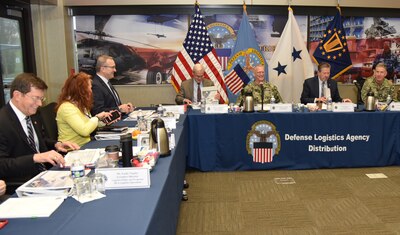 DLA leaders are assembled behind center-facing tables in a conference room