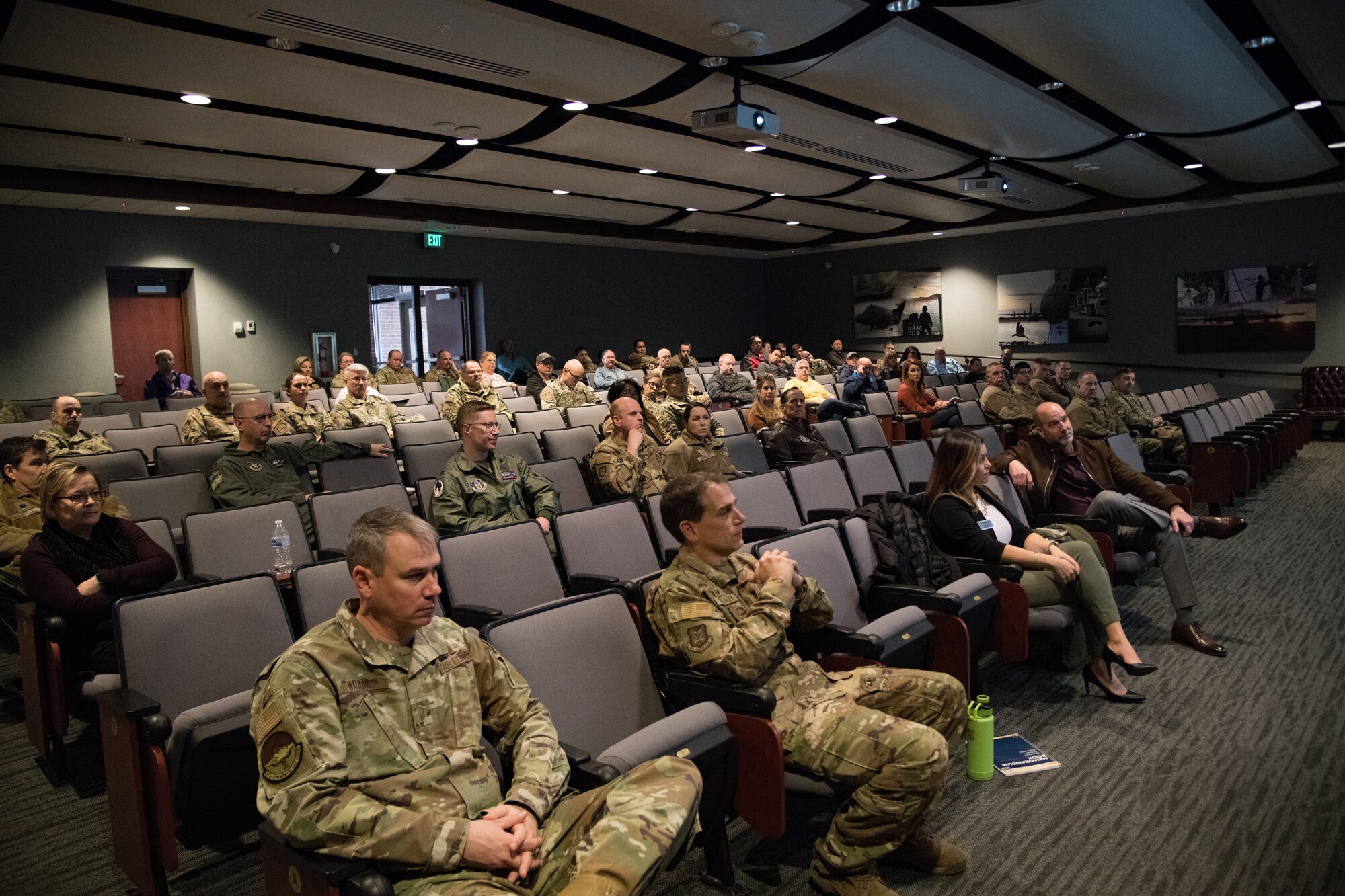 A group of people in a theater wearing a mix of OCP and civilian clothes.