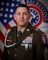 man wearing u.s. army uniform standing in front of 2 flags.