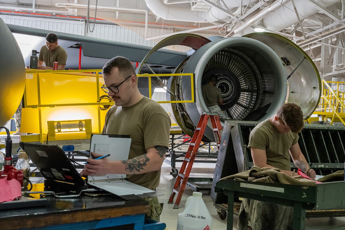 Two Airmen work looks through folders in front of a KC-135 in a maintenance hangar.