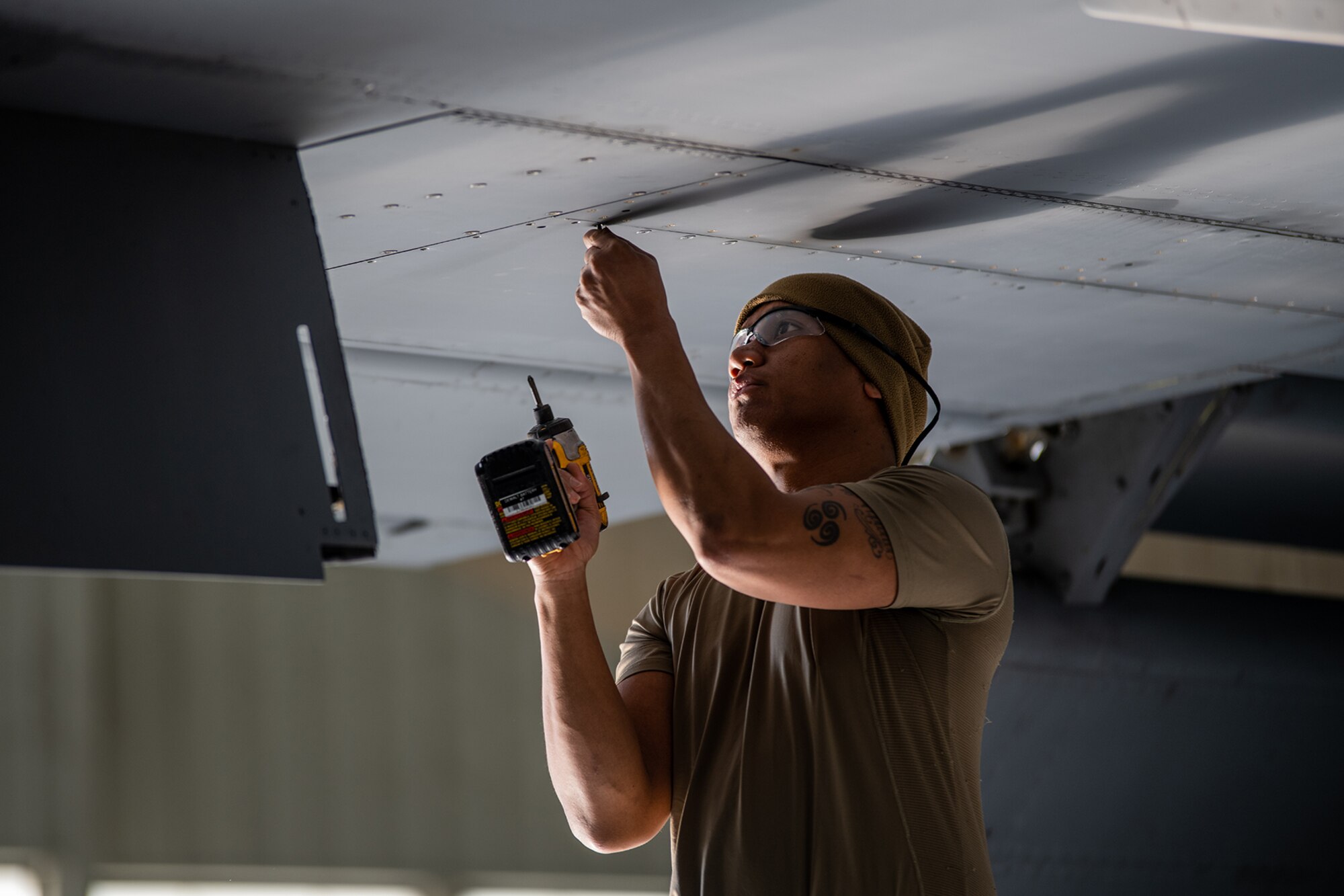 An aircraft maintainer removes a screw with a power drill from below a KC-135 wing.