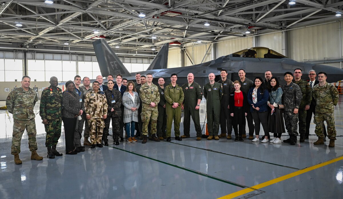 U.S. Air Force personnel, international air attachés and spouses pose for a photo in front of an F-22 Raptor