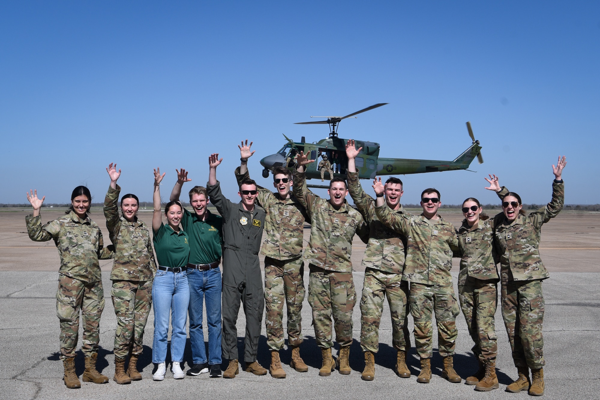 ROTC cadets cheer in front of flying Huey