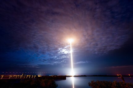 A rocket launches into dark blue, cloudy sky.