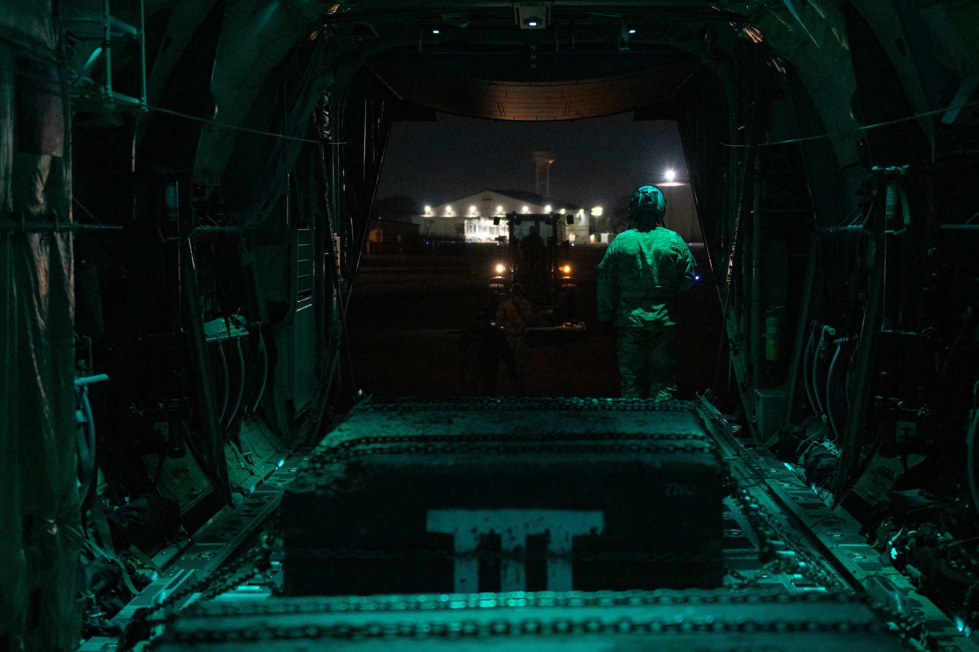 Airman guides a 10K all-terrain forklift to the ramp of a C-130J at night