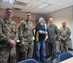 Dave Foland, administrative support technician, Portland MEPS, (center) is presented with the Western Sector Coin for Excellence by Marine Corps Col. Jesse Sjoberg, USMEPCOM Western Sector commander. Foland was recognized for intervening and disarming a possible active shooter in Troutdale, Ore.