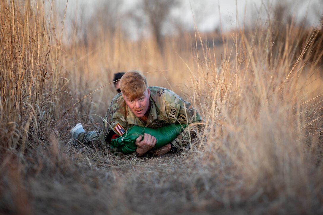 A soldier crawls through a dry, grassy field.