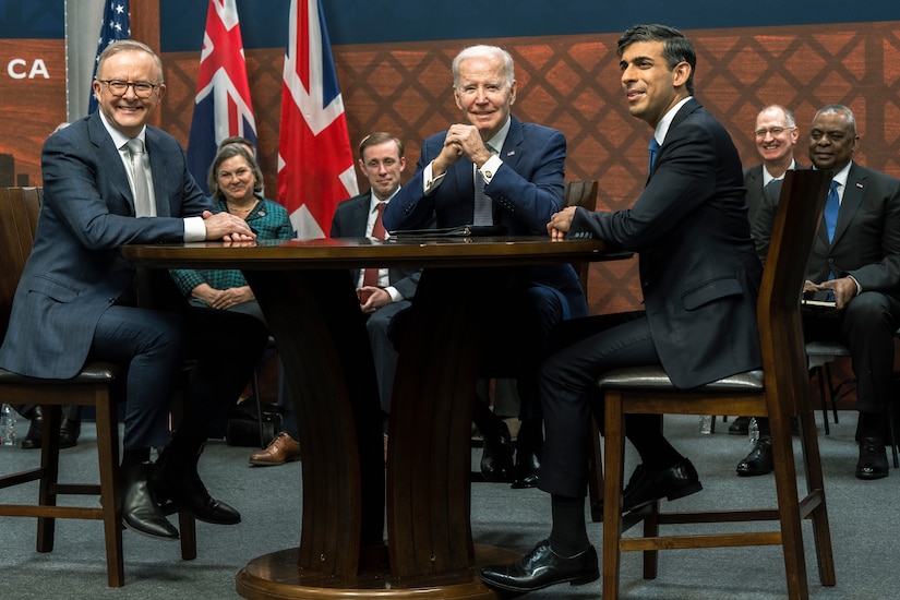 Three men sit around a table and smile for the camera.